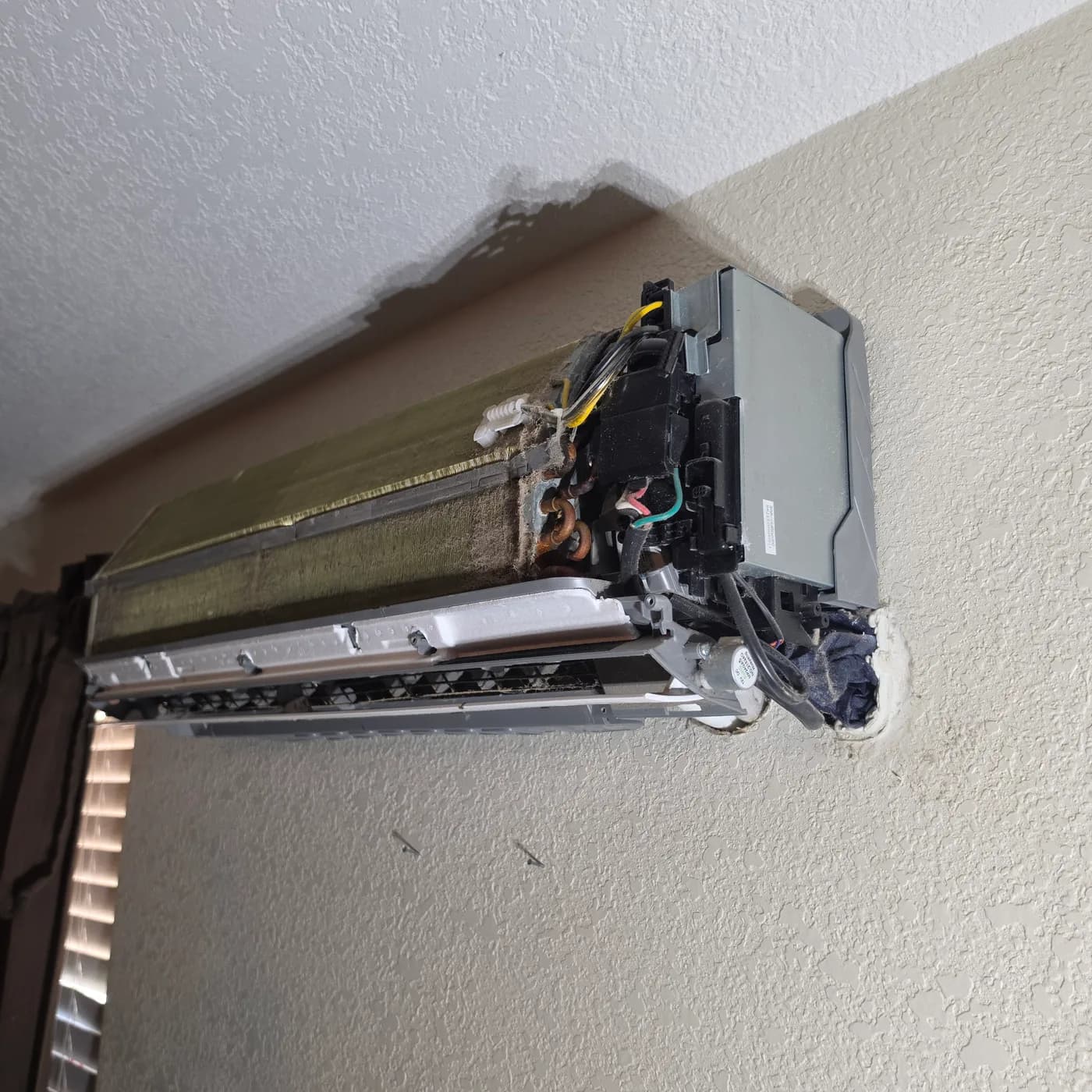 Wall-mounted mini split indoor head opened up with blower wheel removed exposing the coil and wiring for cleaning