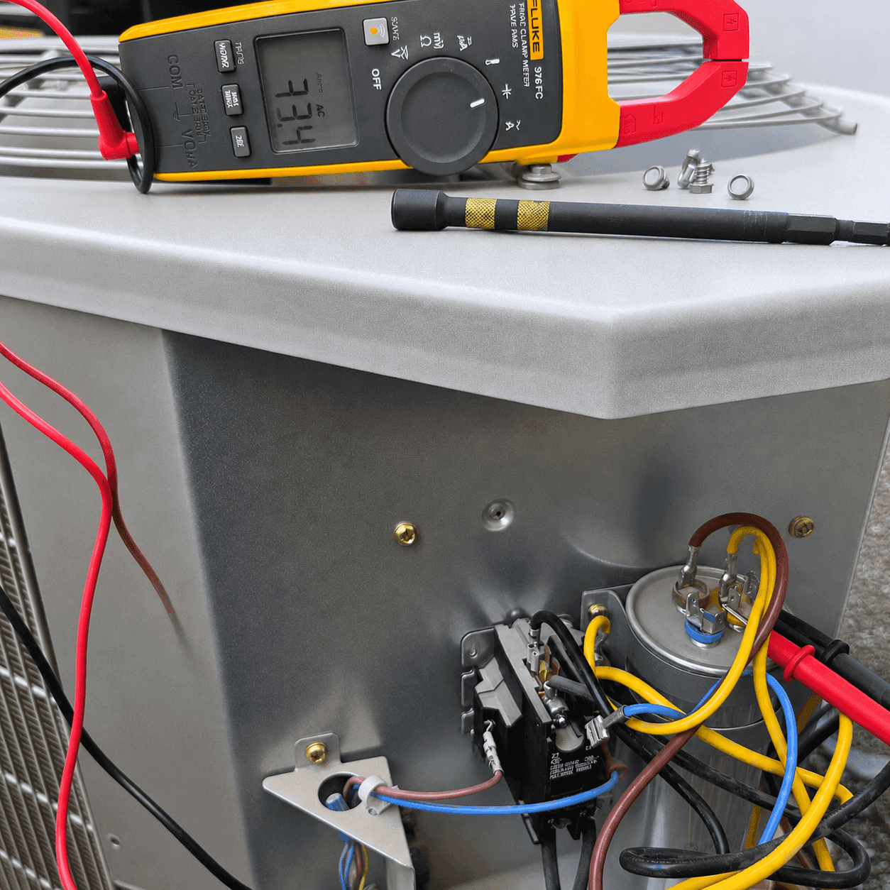 Technician testing an AC run capacitor with a Fluke clamp meter on an outdoor condenser unit in Vail, Arizona