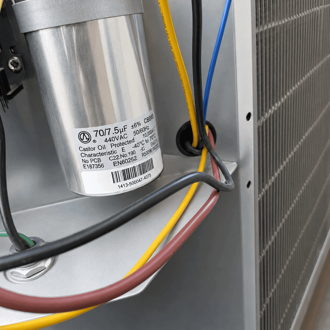 Close-up of a dual run capacitor rated 70/7.5 microfarads at 440 volts wired inside an AC condenser unit