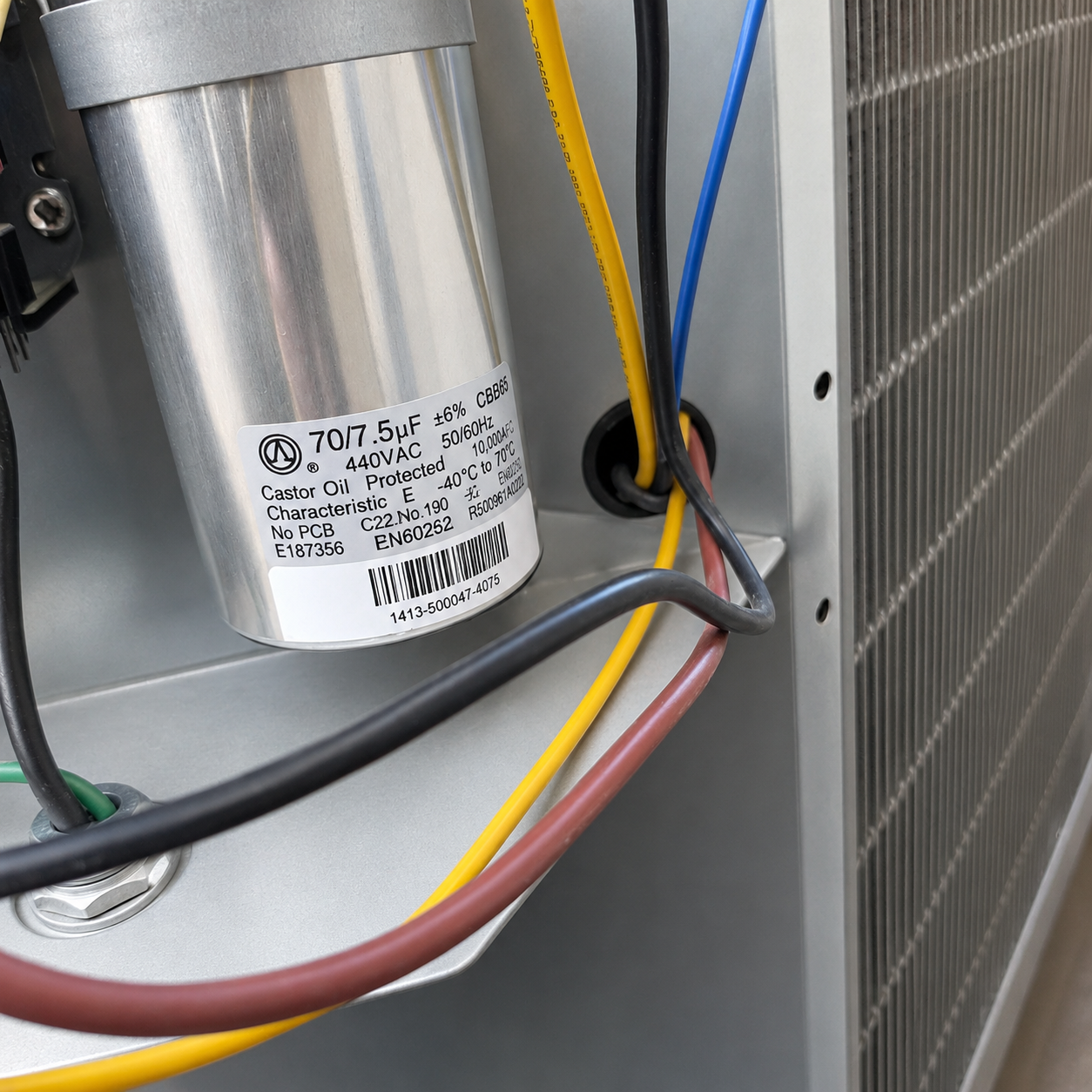 Close-up of a dual run capacitor rated 70/7.5 microfarads at 440 volts wired inside an AC condenser unit
